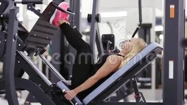 漂亮的女孩穿着黑色运动服，在健身房的腿部按压马什尼上做运动。 保健和福利。